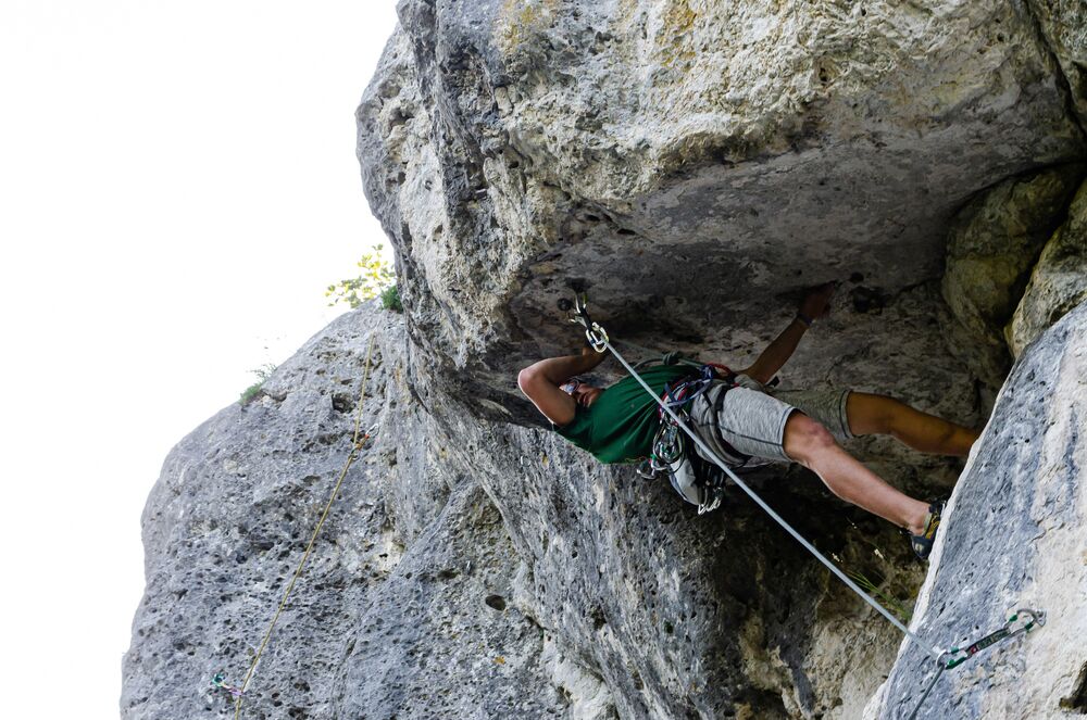 На фотографии парень взбирается на скалу